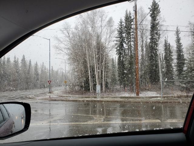 view out a car window of falling snow and a wet road